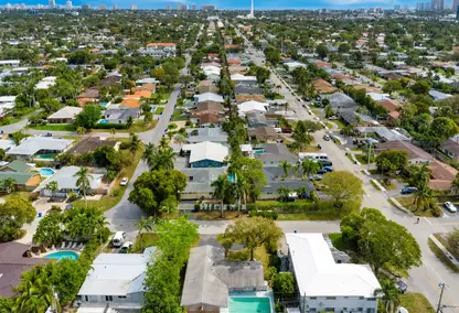 Aerial view of Coral Ridge Isles in Fort Lauderdale, FL with homes, palm-lined streets, pools, and South Florida skyline.